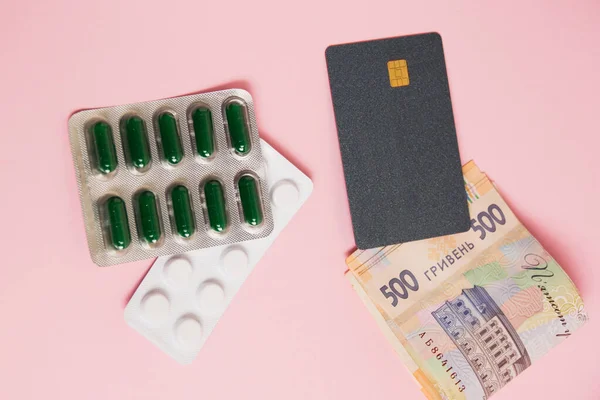 Flatlay, pills, money and bank card on a pink background. Concept of ordering medicine online.