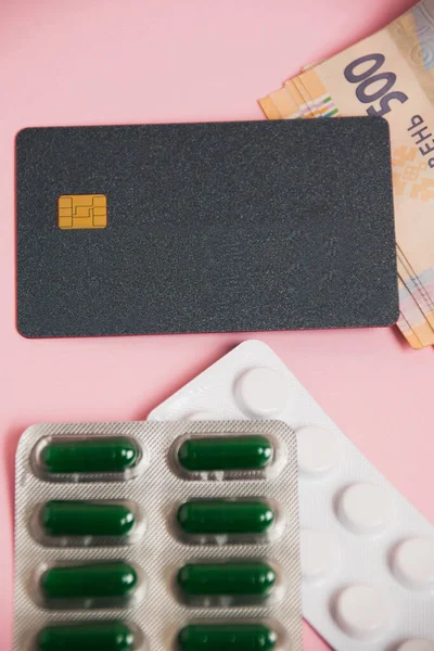 Flatlay, pills, money and bank card on a pink background. Concept of ordering medicine online.