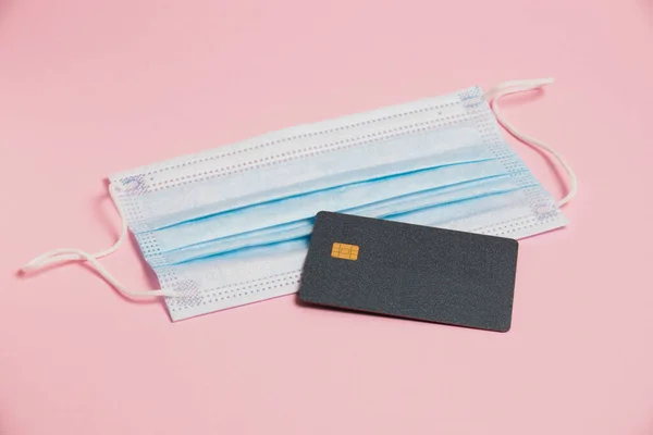 Medical mask and bank card on pink background. Online payment concept for products and medicine.
