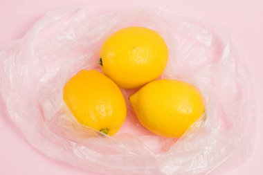 Limonlar plastik torba içinde, arka planda pembe kağıt üzerinde fotokopi alanı var. Toprak günü kavramı, sıfır atık ve geri dönüşüm