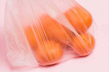 Pembe bir arka planda plastik poşette mandalinalar. Toprak günü kavramı, sıfır atık ve geri dönüşüm