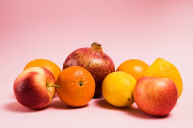 Pembe arka planda nar, limon, elma, portakal ve mandalina meyveleri. Parlak bir arka planda lezzetli meyveler