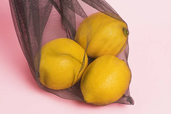 Lemons in a reusable net for fruits and vegetables on a pink background. Concept of earth day, zero waste and recycling