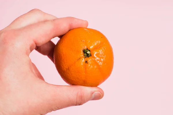 stock image Tangerine in female hand on pink paper background with copy space