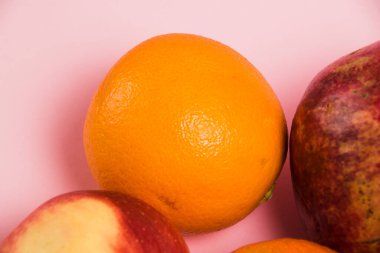Pembe arka planda sulu portakal, elma ve nar. Parlak bir arka planda lezzetli meyveler