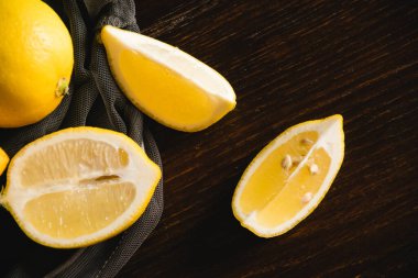 Düz döşeme, meyve ağındaki limonlar, koyu arkaplanda sulu limon parçaları. Dünya günü ve sıfır atık kavramı.