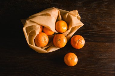 Toprak günü kavramı, geri dönüşüm ve sıfır atık. Koyu arkaplanda meyve ve sebzeler için tekrar kullanılabilir kahverengi bir çantada tatlı mandalinalar..