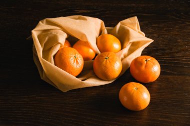 Toprak günü kavramı, geri dönüşüm ve sıfır atık. Koyu arkaplanda meyve ve sebzeler için tekrar kullanılabilir kahverengi bir çantada tatlı mandalinalar..