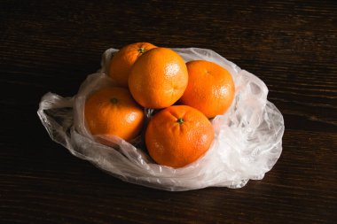 Toprak günü kavramı, geri dönüşüm ve sıfır atık. Siyah arka planda plastik bir torba içinde tatlı mandalinalar.