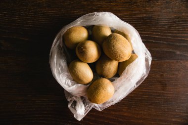 Toprak günü kavramı, geri dönüşüm ve sıfır atık. Koyu arkaplanda plastik poşette tatlı kivi.