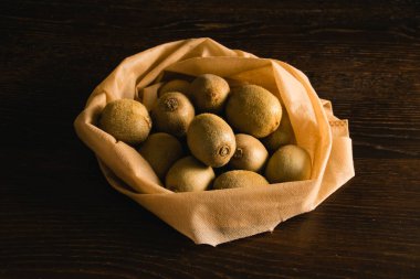 Toprak günü kavramı, geri dönüşüm ve sıfır atık. Koyu bir arka planda meyve ve sebze için yeniden kullanılabilir bir poşette tatlı kivi.