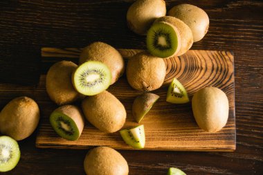 Karanlık bir arka planda tatlı meyve. Bütün kivi ve parçalar tahta bir kesme tahtasının üzerinde.