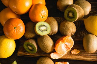 Flatlay, arka planda tatlı meyve. Mandalina, limon, kivi, ahşap kesim tahtasındaki bütün meyve ve parçalar.