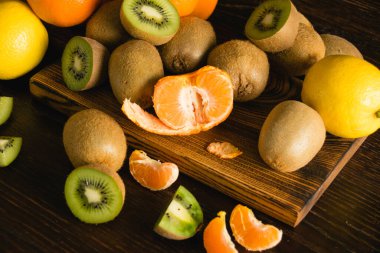 Flatlay, arka planda tatlı meyve. Mandalina, limon, kivi, ahşap kesim tahtasındaki bütün meyve ve parçalar.
