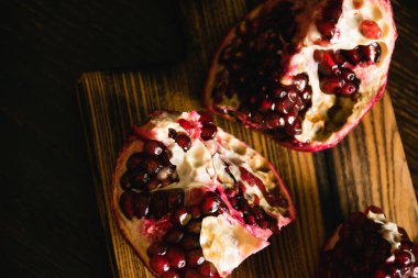 Koyu arkaplanda kesme tahtasındaki nar parçaları..