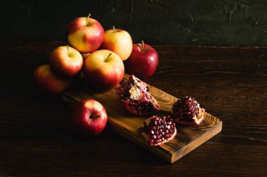 Koyu arkaplanda meyveler. Kesme tahtasında tatlı nar ve kırmızı elma parçaları.
