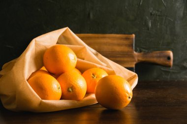 Toprak günü kavramı, gübreleme, sıfır atık ve geri dönüşüm. Sebzeler için yeniden kullanılabilir bir çantada portakallar ve arka planda meyveler ve ahşap kesim tahtası.