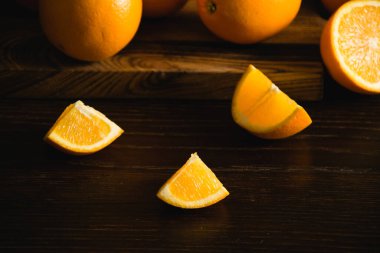 Portakallar bir bütün ve siyah arka planda ahşap bir kesme tahtasının üzerinde parçalar halinde..