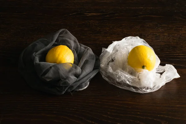 Earth day, recycling and zero waste concept. Fruits in a plastic bag and in a reusable net, lemons on a dark wooden background