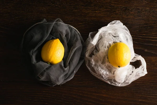 Earth day, recycling and zero waste concept. Fruits in a plastic bag and in a reusable net, lemons on a dark wooden background