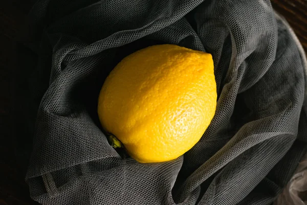 Earth day, recycling and zero waste concept. Lemons in a reusable mesh for fruits and vegetables on a dark background.