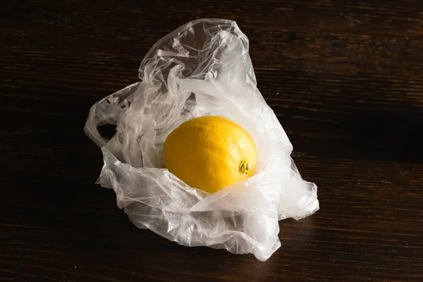 Earth day, recycling and zero waste concept. Lemon in a plastic bag on a dark background.