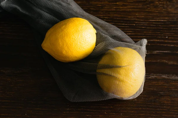 Earth day, recycling and zero waste concept. Lemons in a reusable mesh for fruits and vegetables on a dark background.