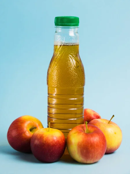 Apple juice in a plastic bottle and red apples on a blue background. Earth day, zero waste and plastic recycling concept