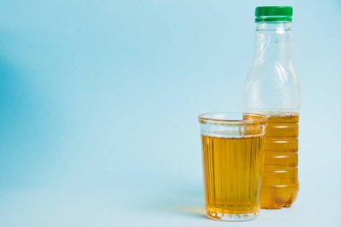 Mavi kağıdın üzerinde bir bardak meyve suyu ve plastik şişe. Toprak günü kavramı, sıfır atık ve plastik geri dönüşümü