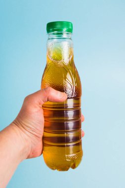 Mavi arka plandaki birinin elinde içki olan plastik bir şişe. Toprak günü kavramı, sıfır atık ve plastik geri dönüşümü