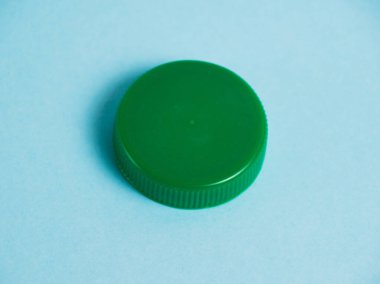 Mavi arka planda yeşil plastik şişe kapağı. Toprak günü kavramı, sıfır atık ve plastik geri dönüşümü