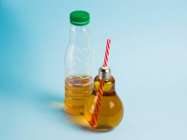 Yarı boş plastik şişe, içki ve meyve suyu mavi arka planda yeniden kullanılabilir cam şişede. Toprak günü kavramı, sıfır atık ve plastik geri dönüşümü