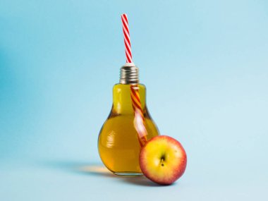 Elma suyu, mavi arka planda pipetle yeniden kullanılabilir cam bir şişede. Toprak günü kavramı, sıfır atık ve plastik geri dönüşümü