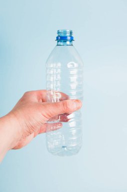 Mavi kağıt arka planda insan elinde kullanılmış plastik şişe. Toprak günü kavramı, sıfır atık ve plastik geri dönüşümü
