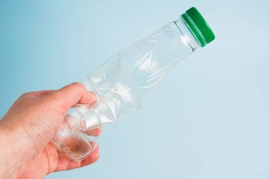 Mavi kağıt arka planda insan elinde kullanılmış plastik şişe. Toprak günü kavramı, sıfır atık ve plastik geri dönüşümü