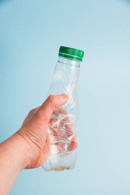 Mavi kağıt arka planda insan elinde kullanılmış plastik şişe. Toprak günü kavramı, sıfır atık ve plastik geri dönüşümü