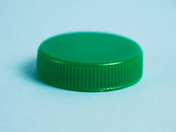 stock image Green plastic bottle cap on a blue background. Concept of earth day, zero waste and plastic recycling