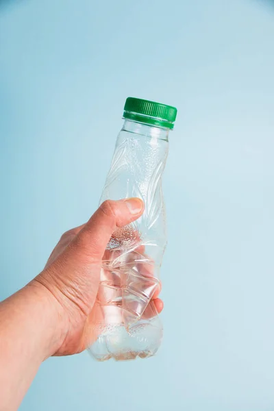 Used plastic bottle in human hand on blue paper background. Concept of earth day, zero waste and plastic recycling