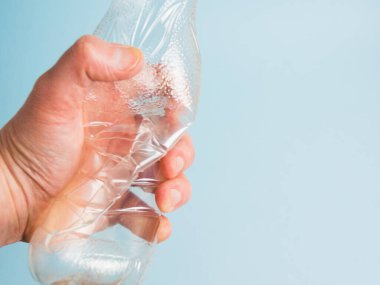 Mavi kağıt arka planda insan elinde kullanılmış plastik şişe. Toprak günü kavramı, sıfır atık ve plastik geri dönüşümü