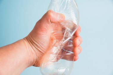 Mavi kağıt arka planda insan elinde kullanılmış plastik şişe. Toprak günü kavramı, sıfır atık ve plastik geri dönüşümü