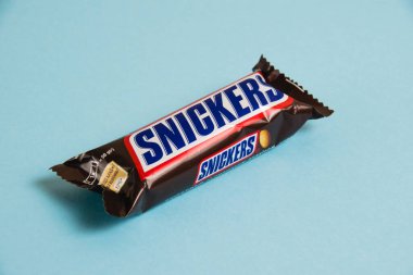 Ukrayna, Chernihiv, 26 Nisan 2023: Lezzetli Snickers çikolatası mavi arka planda yer fıstığı paketinde.