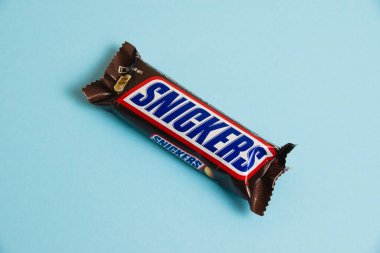 Ukrayna, Chernihiv, 26 Nisan 2023: Lezzetli Snickers çikolatası mavi arka planda yer fıstığı paketinde.