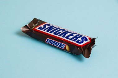 Ukrayna, Chernihiv, 26 Nisan 2023: Lezzetli Snickers çikolatası mavi arka planda yer fıstığı paketinde.