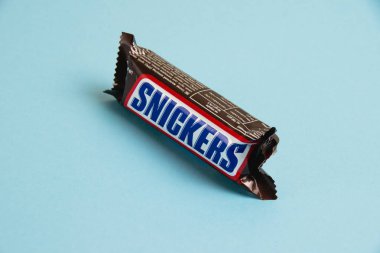 Ukrayna, Chernihiv, 26 Nisan 2023: Lezzetli Snickers çikolatası mavi arka planda yer fıstığı paketinde.