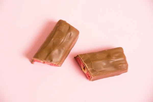 stock image Pieces of appetizing chocolate bar with whole nut and strawberry on a pink background.