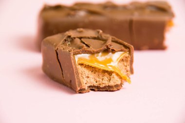 Pembe arka planda karamel makrosu olan çikolata parçaları..