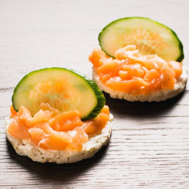 Kırmızı balık ve salatalıklı sandviç. Ahşap zemin üzerinde gevrek pirinç ekmeğine tuzlanmış somon balığı..