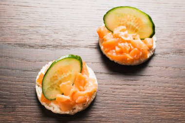 Kırmızı balık ve salatalıklı sandviç. Ahşap zemin üzerinde gevrek pirinç ekmeğine tuzlanmış somon balığı..