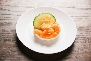 Kırmızı balıklı sandviç ve beyaz tabakta yakın plan salatalık. Ahşap zemin üzerinde gevrek pirinç ekmeğine tuzlanmış somon balığı..