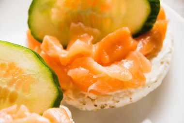 Kırmızı balıklı sandviç ve beyaz tabakta salatalık, yakın plan. Çıtır pirinç ekmeğine tuzlanmış somon balığı.